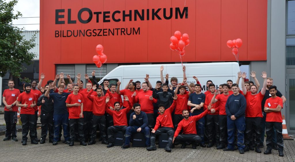 Gruppenbild aller Auszubildenden in Dienstkleidung vor dem ELOTechnikum Bildngszentrum der ELOMECH-GRUPPE am Hauptsitz in Mülheim an der Ruhr.